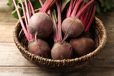 Raw ripe beets in wicker bowl on wooden table, closeup