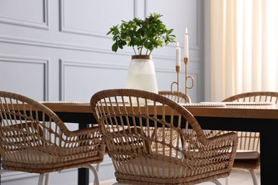 Photo of Rattan chairs, table, burning candles and vase with green branches in stylish dining room