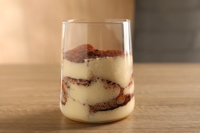 Photo of Delicious tiramisu in glass on wooden table, closeup