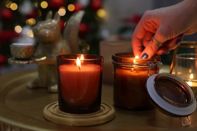 Woman lighting candle in room decorated for Christmas, closeup