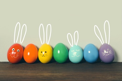 Image of Several eggs with drawn faces and ears as Easter bunnies among others on wooden table against light grey background