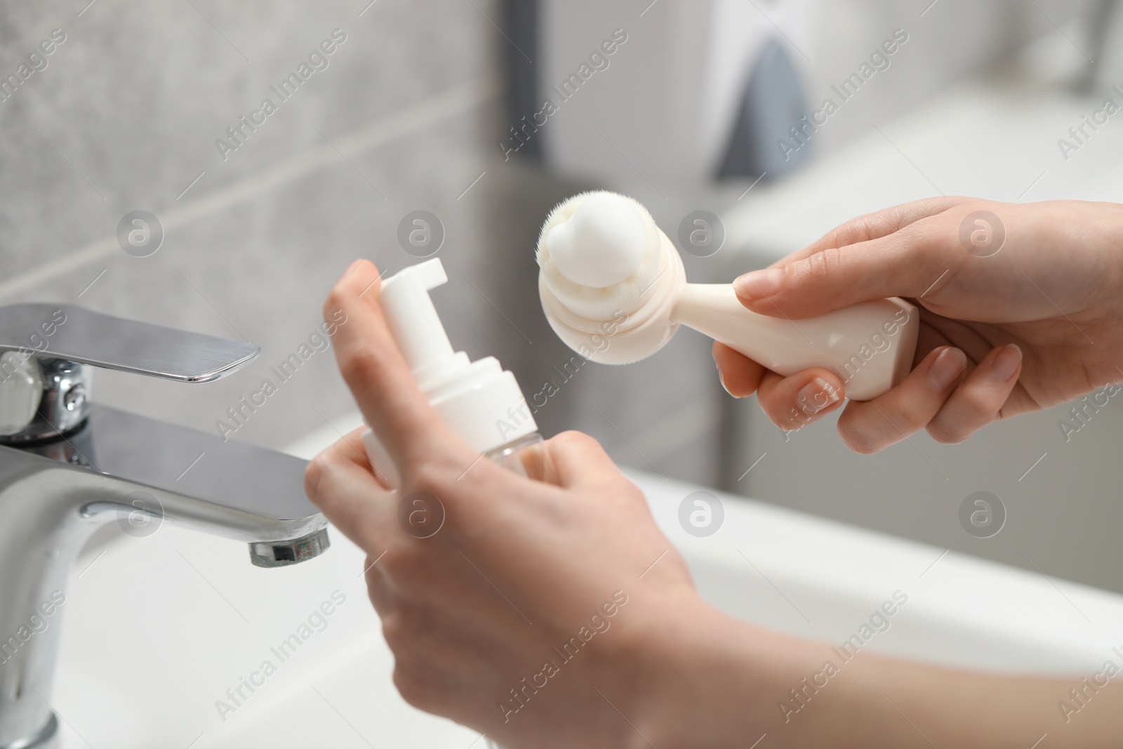 Photo of Washing face. Woman applying cleansing foam onto brush above sink in bathroom, closeup