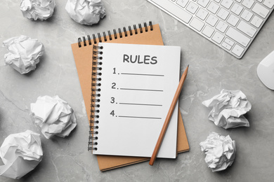 Notebook with list of rules and crumpled paper balls on grey marble table, flat lay