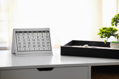 Photo of Paper calendar and bonsai tree on white table indoors