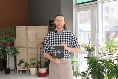 Photo of Male florist holding OPEN sign at workplace