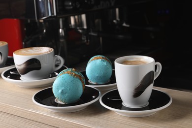 Cups of fresh aromatic coffee and delicious macarons on wooden counter in cafe