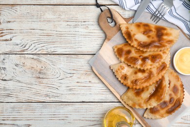 Photo of Delicious fried chebureki with sauce on white wooden table, flat lay. Space for text