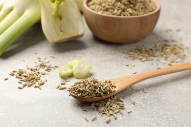 Photo of Spoon with fennel seeds and cut vegetable on light gray table, closeup