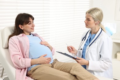 Photo of Doctor with clipboard consulting smiling pregnant patient in clinic