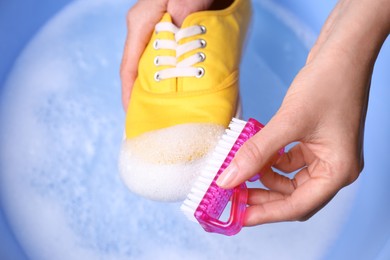 Woman washing shoe with brush in basin, closeup