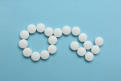 Photo of Male sign with bent arrow of white pills symbolizing potency problems on light blue background, flat lay