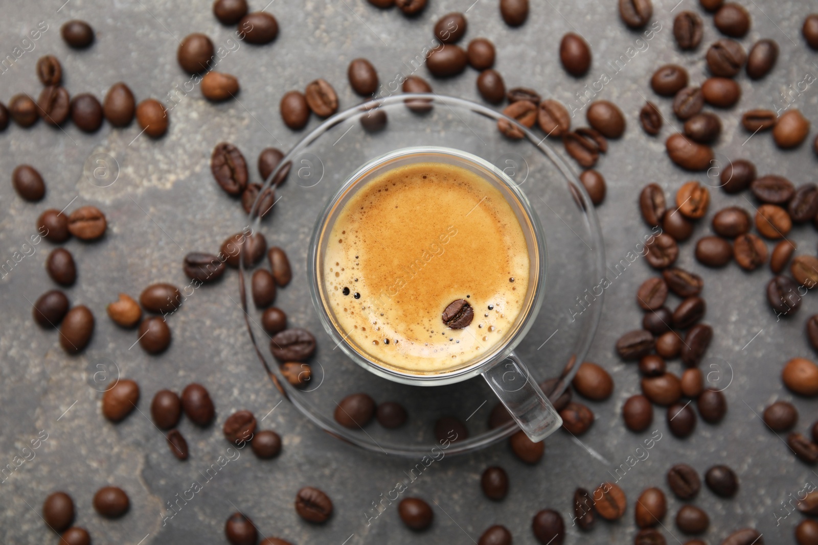 Photo of Cup of tasty espresso and scattered coffee beans on grey table, flat lay
