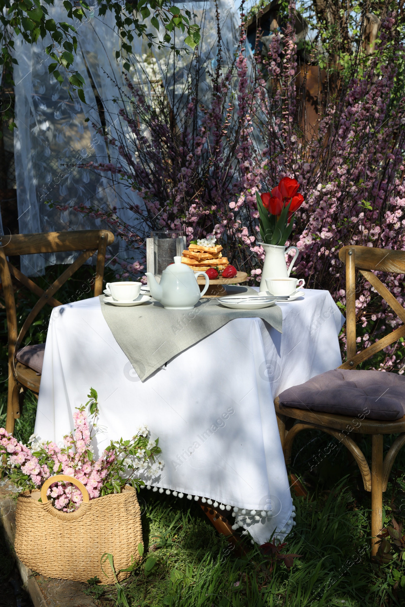 Photo of Beautiful bouquet of tulips and freshly baked waffles on table served for tea drinking in garden