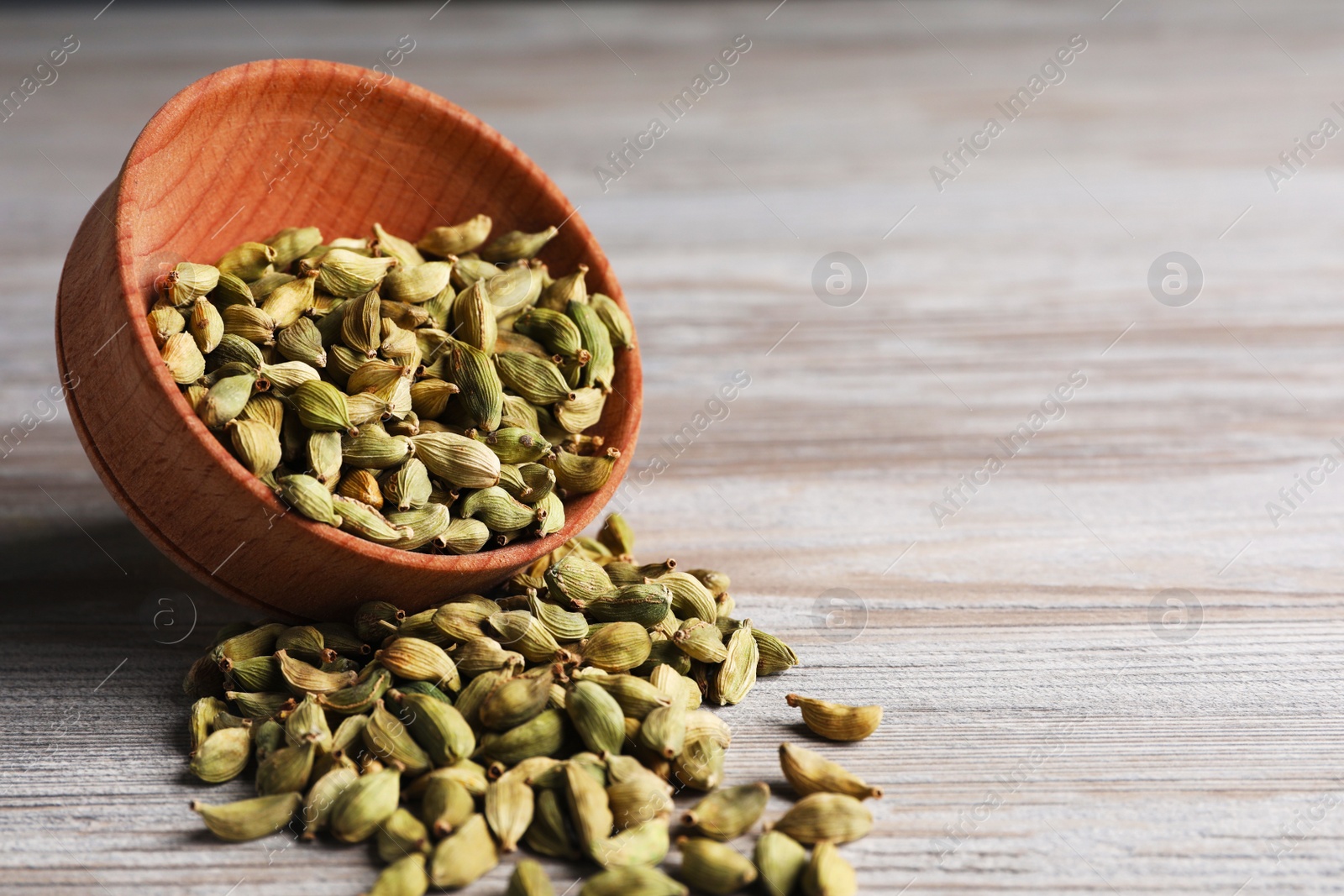 Photo of Overturned bowl with dry cardamom pods on wooden table, closeup. Space for text