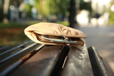 Photo of Beige leather purse on wooden bench outdoors, closeup. Lost and found