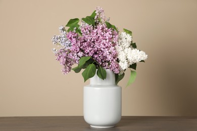 Beautiful lilac flowers in vase on wooden table against beige background