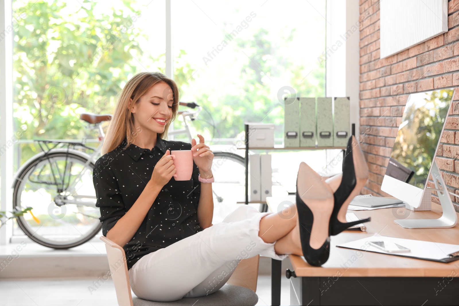 Photo of Happy young businesswoman with cup of coffee enjoying peaceful moment at workplace