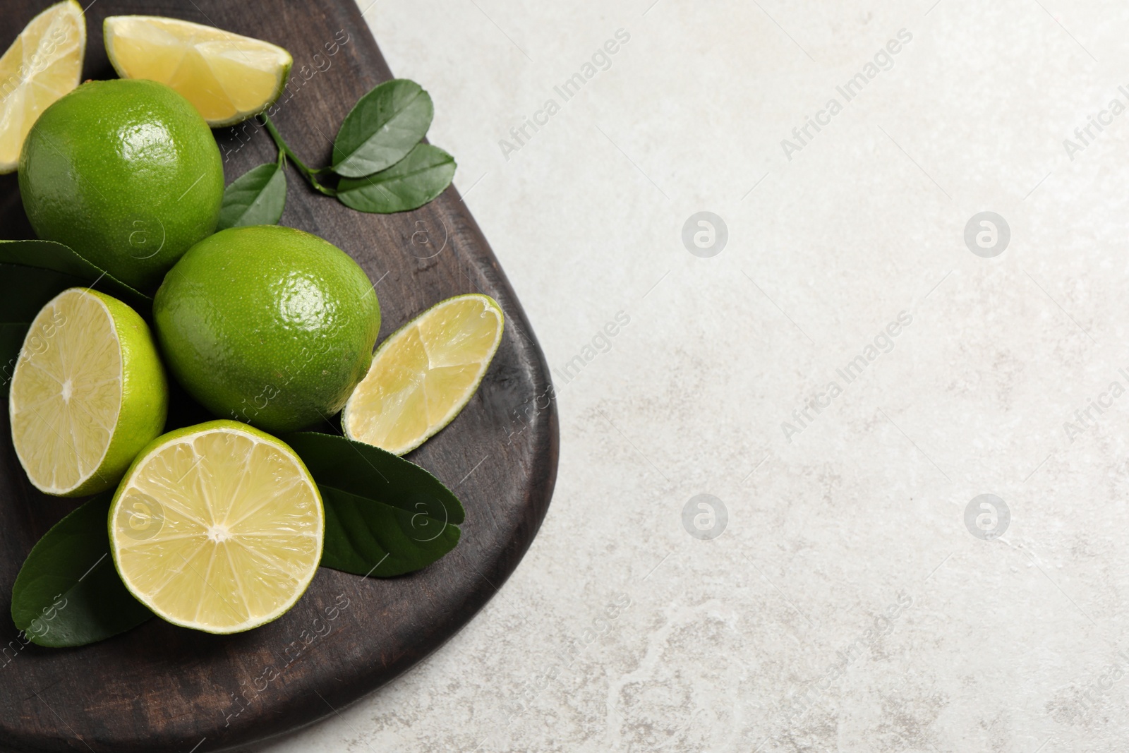 Photo of Fresh limes and green leaves on light table, top view. Space for text