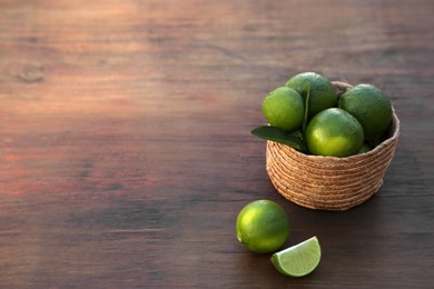 Photo of Fresh ripe limes and wicker basket on wooden table. Space for text