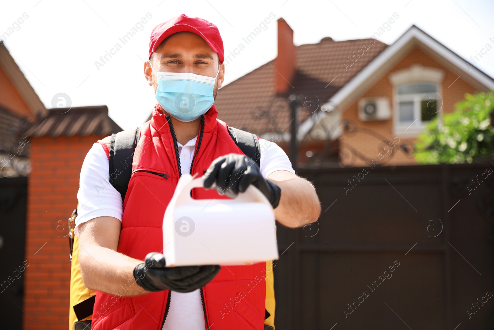 Photo of Courier in protective mask and gloves with order outdoors. Restaurant delivery service during coronavirus quarantine