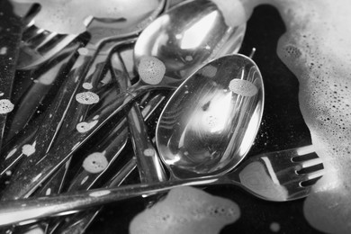 Washing silver spoons, forks and knives in water with foam, closeup