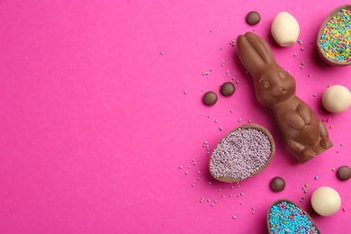 Flat lay composition with chocolate Easter bunny, candies and eggs on pink background. Space for text