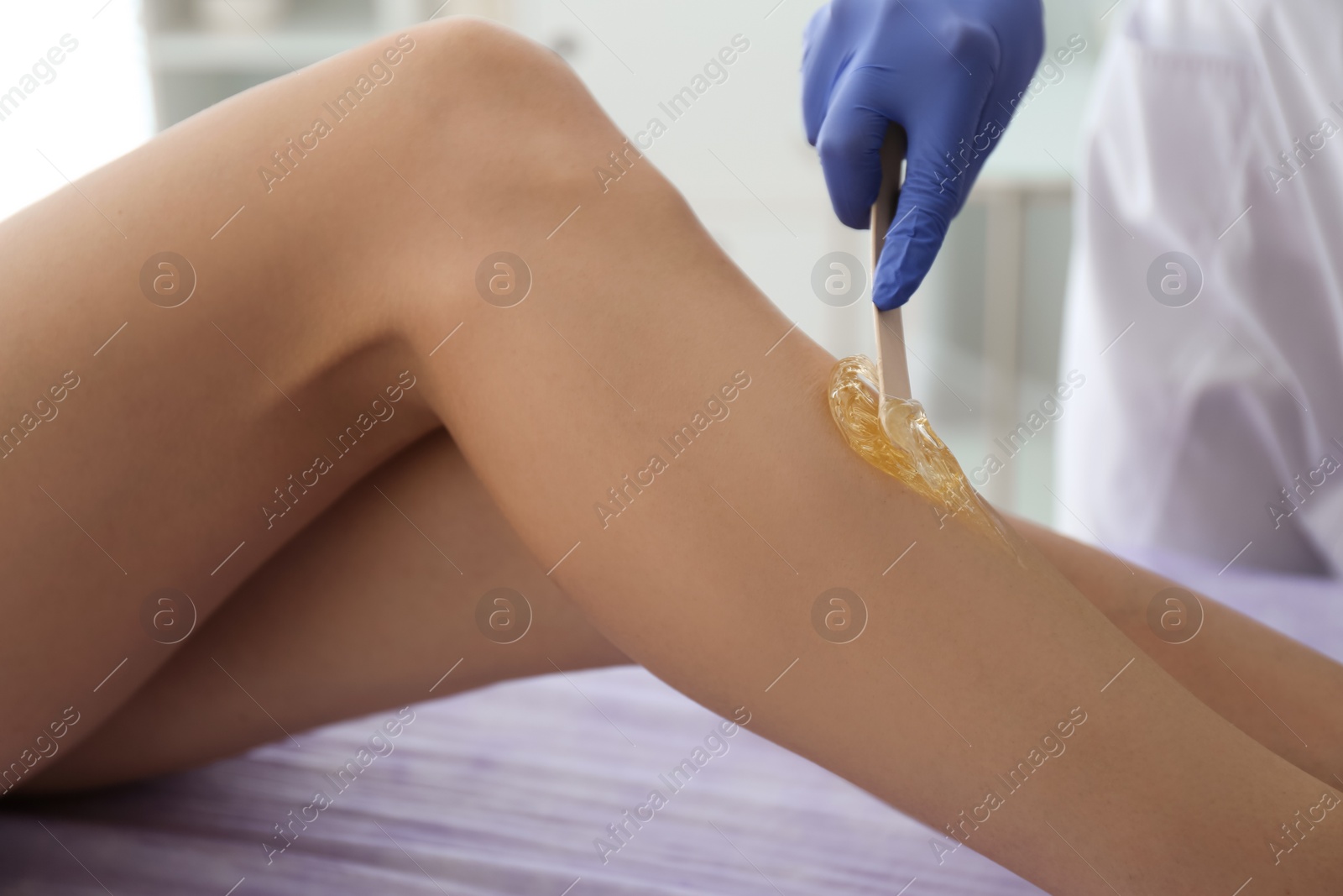 Photo of Woman getting wax epilation of legs in salon, closeup