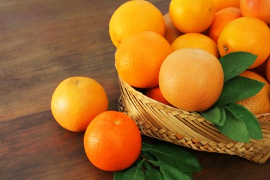 Photo of Wicker basket with different citrus fruits and leaves on wooden table, closeup