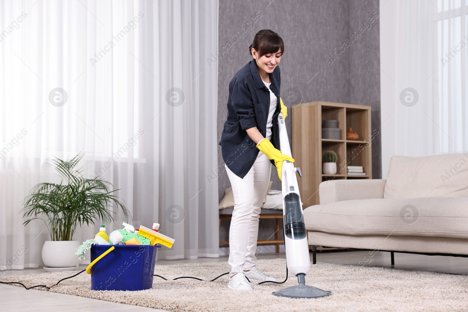 Photo of Happy young housewife vacuuming carpet at home