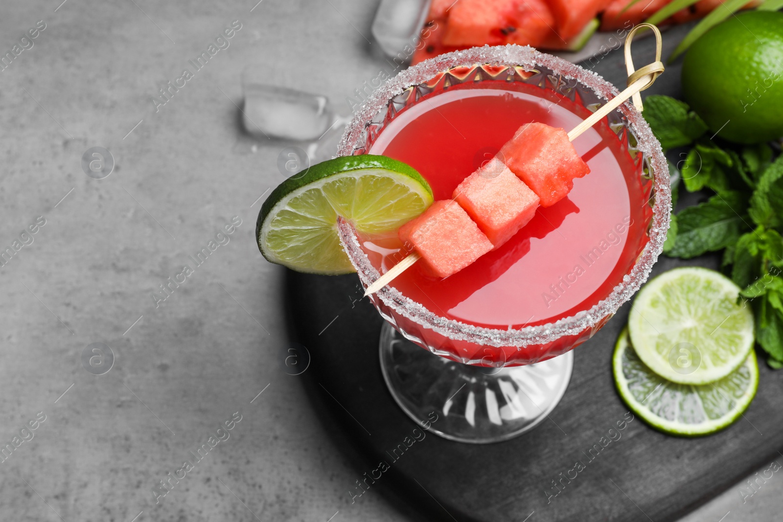 Photo of Cocktail glass of delicious fresh watermelon juice, lime and mint on grey table. Space for text