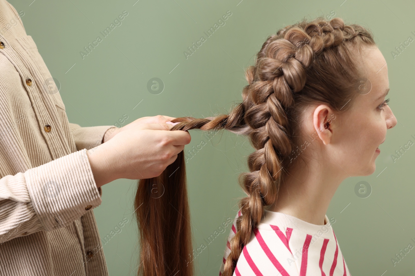 Photo of Professional stylist braiding woman's hair on olive background, closeup