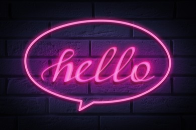 Image of Stylish neon sign with word Hello on brick wall