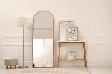 Beautiful mirror, console table and lamp near white wall indoors. Interior design