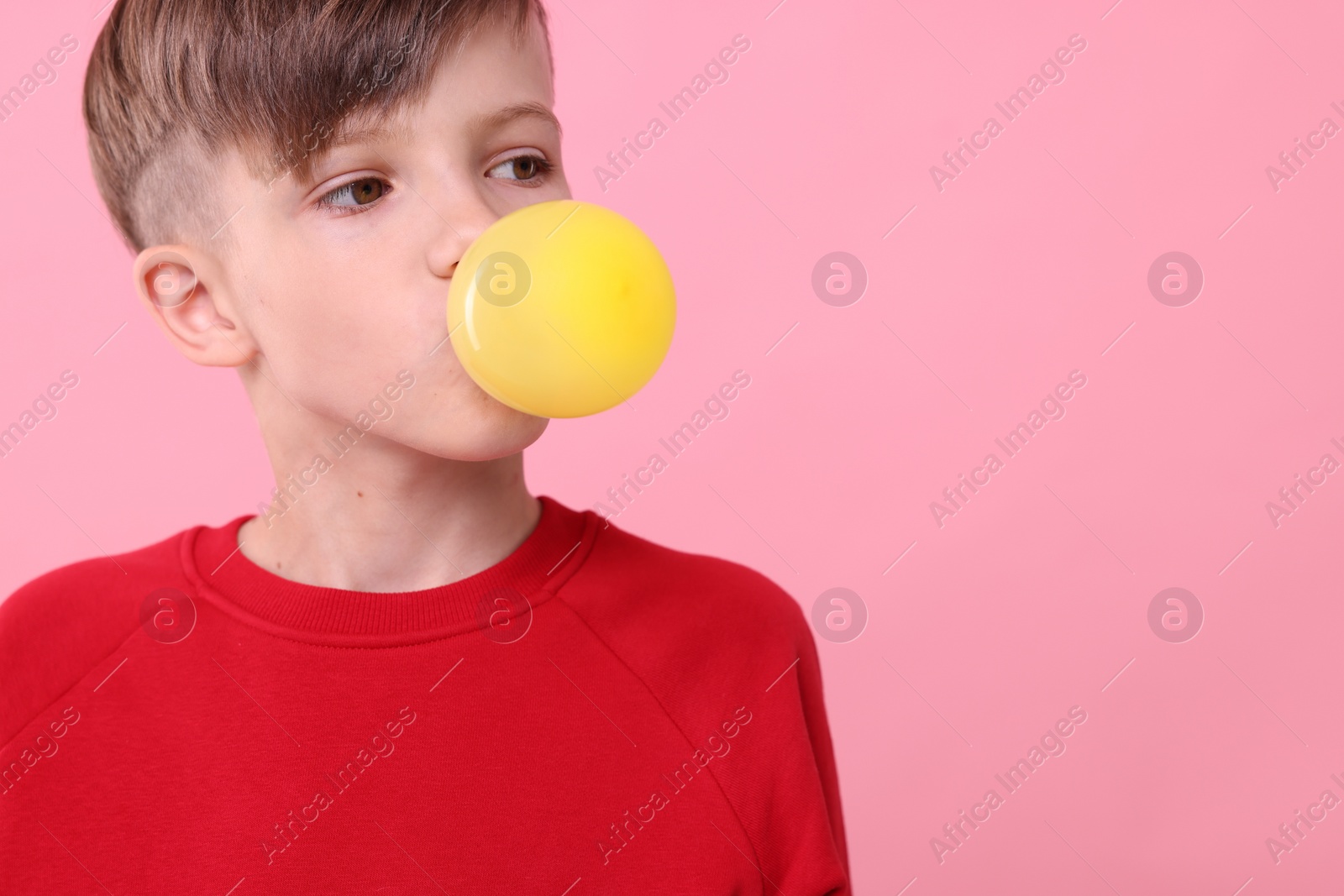 Photo of Boy blowing bubble gum on pink background, space for text