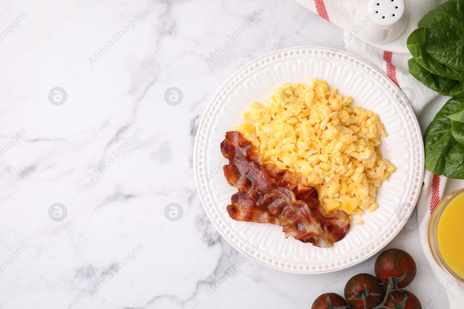 Photo of Delicious scrambled eggs with bacon served on white marble table, flat lay. Space for text