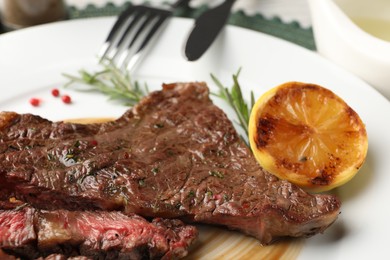 Photo of Delicious grilled beef steak with spices and lemon on plate, closeup