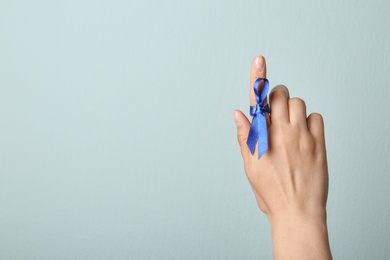 Photo of Woman with blue ribbon on finger against light background, closeup. Symbol of social and medical issues