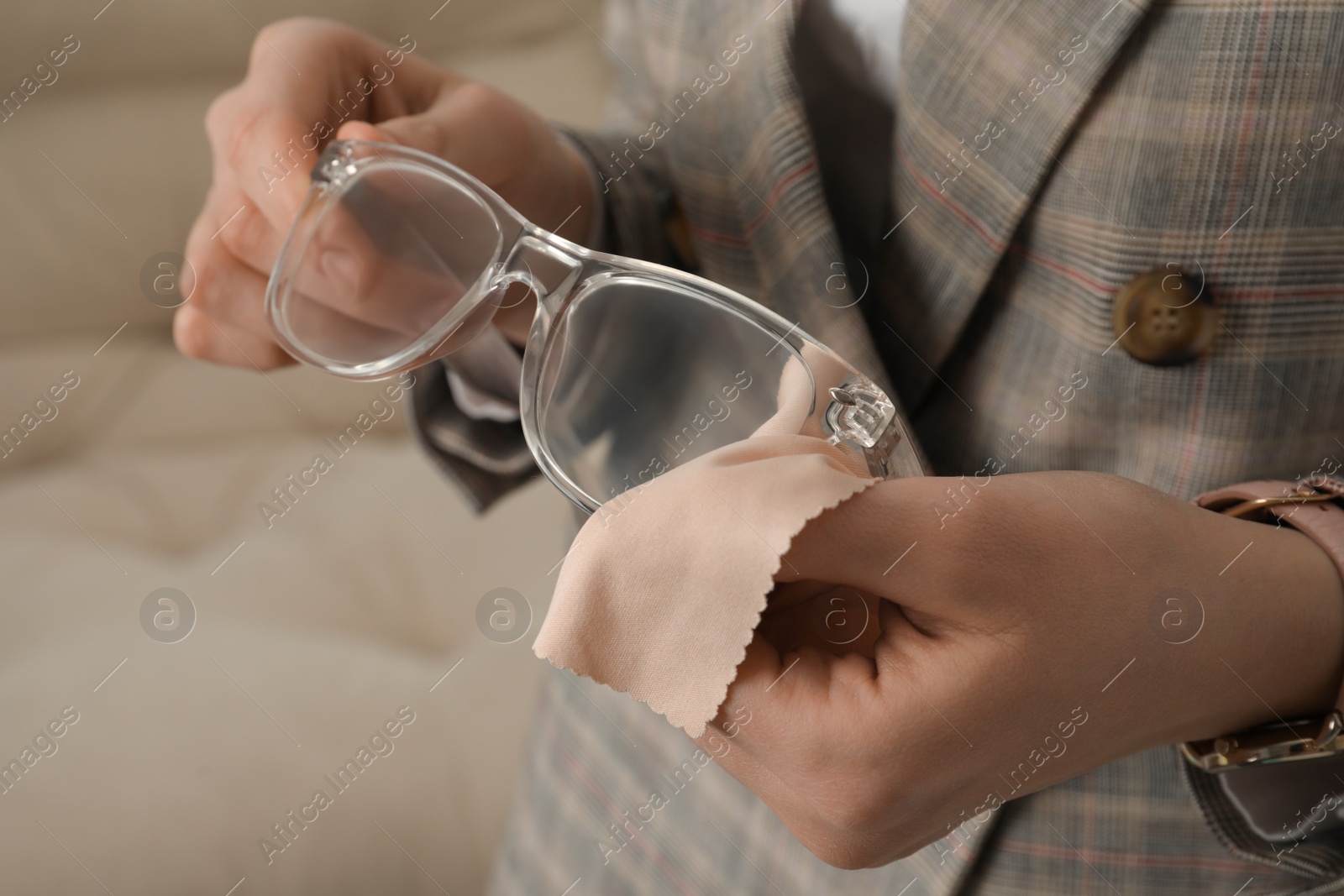 Photo of Woman cleaning glasses with microfiber cloth at home, closeup