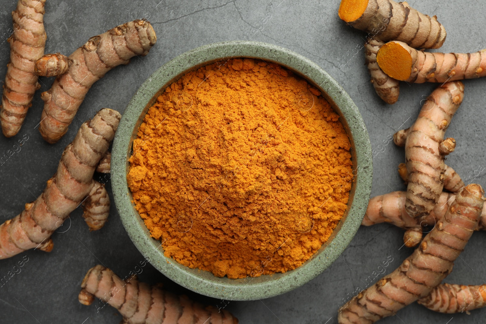 Photo of Bowl with turmeric powder and raw roots on grey table, flat lay