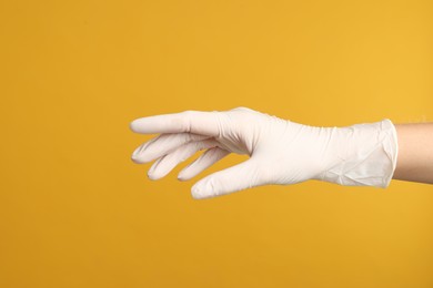 Doctor wearing medical gloves on yellow background, closeup