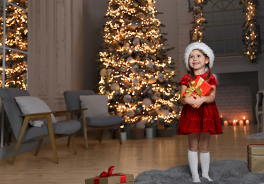 Cute little child wearing Santa hat with Christmas gift in living room