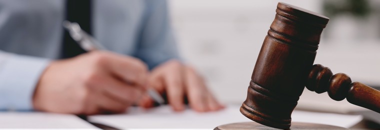 Image of Lawyer working with document at wooden table in office, focus on gavel. Banner design