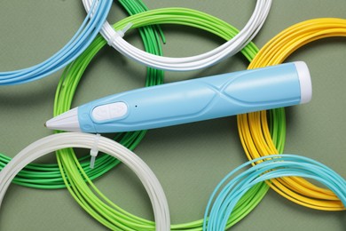 Photo of Stylish 3D pen and colorful plastic filaments on khaki background, flat lay