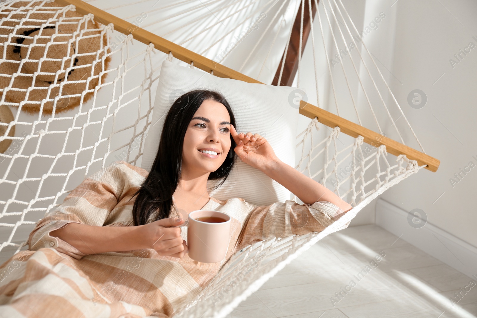 Photo of Young woman with cup of tea in hammock at home