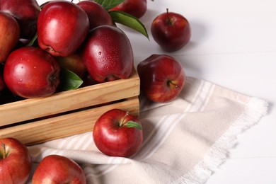 Photo of Fresh red apples with leaves in crate on white wooden table. Space for text