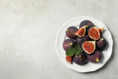 Photo of Whole and cut ripe figs with leaf on light table, top view. Space for text