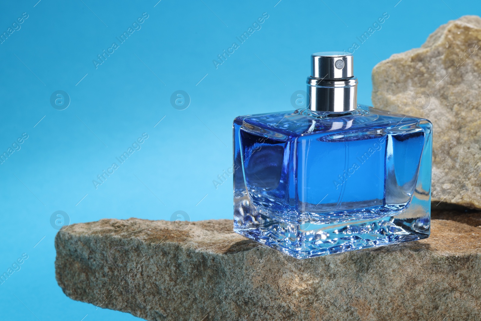 Photo of Stylish presentation of luxury men`s perfume on stones against light blue background. Space for text