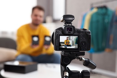 Photo of Fashion blogger showing wristwatches while recording video at home, focus on camera