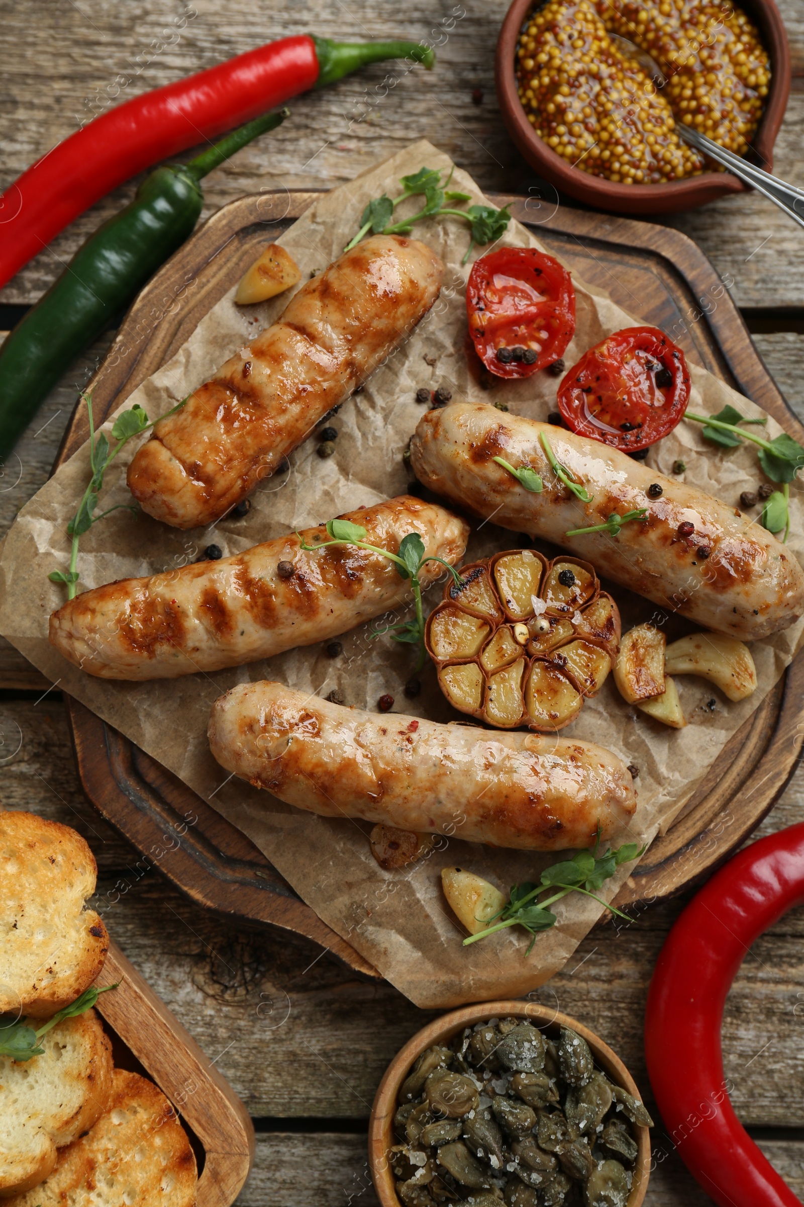 Photo of Tasty fresh grilled sausages with vegetables on wooden table, flat lay