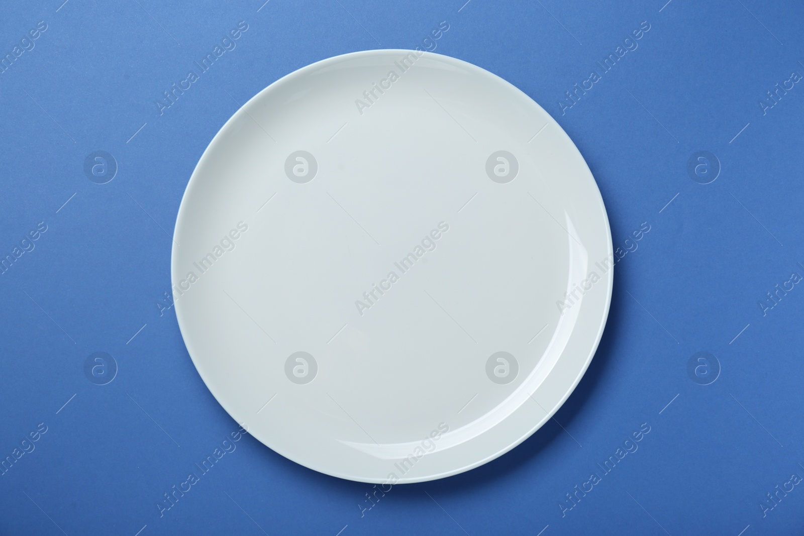 Photo of Empty white ceramic plate on blue background, top view